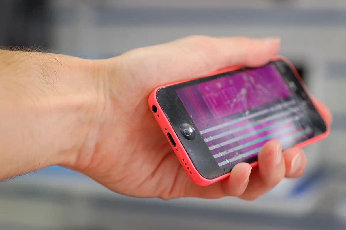 Telefon, jehož displej zobrazuje růžové plochy a vodorovné pruhy — poškozený panel